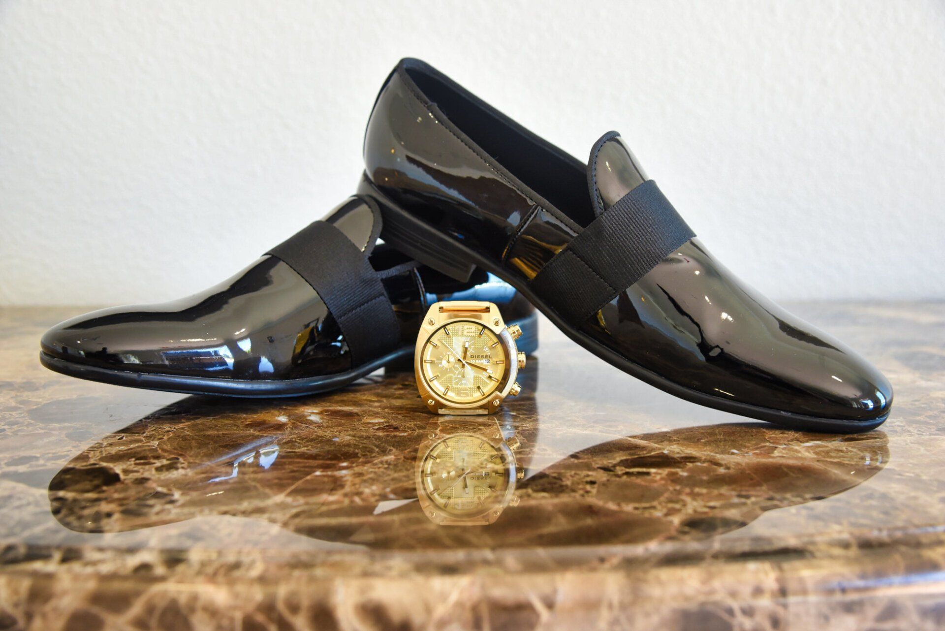 a pair of black shoes and a gold watch are on a table .