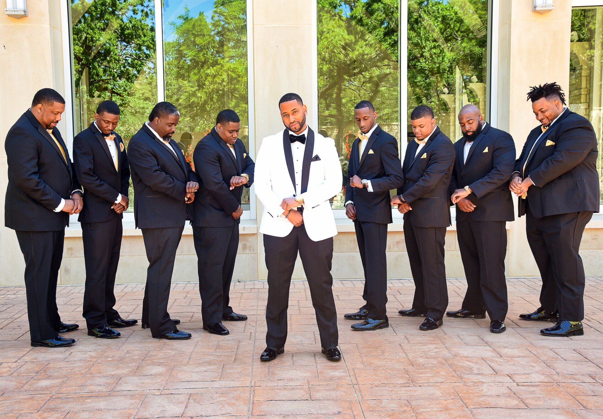 a man in a white tuxedo is standing in front of a group of men in black suits .