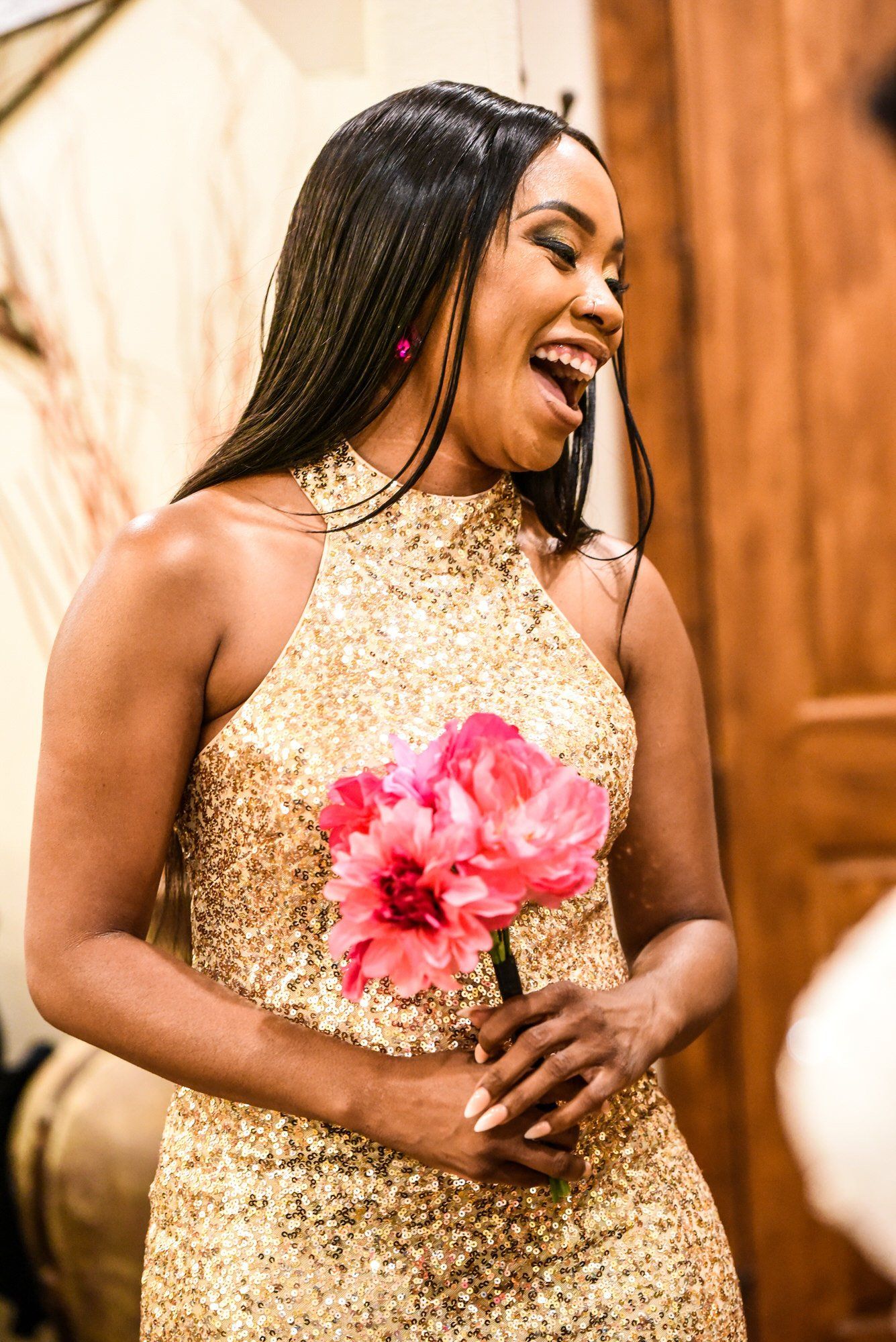a woman in a gold dress is holding a bouquet of pink flowers .