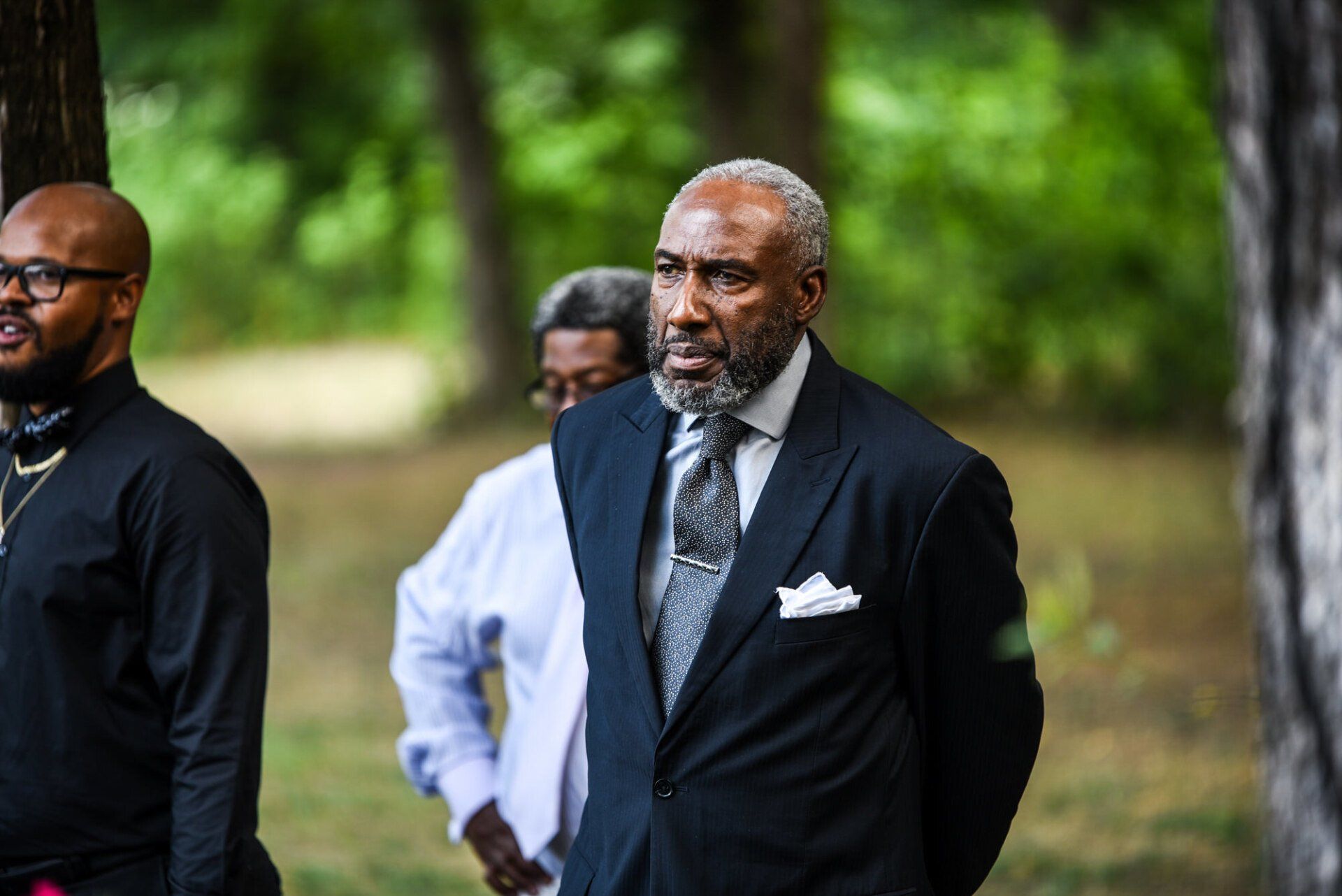 a man in a suit and tie is standing in the woods .