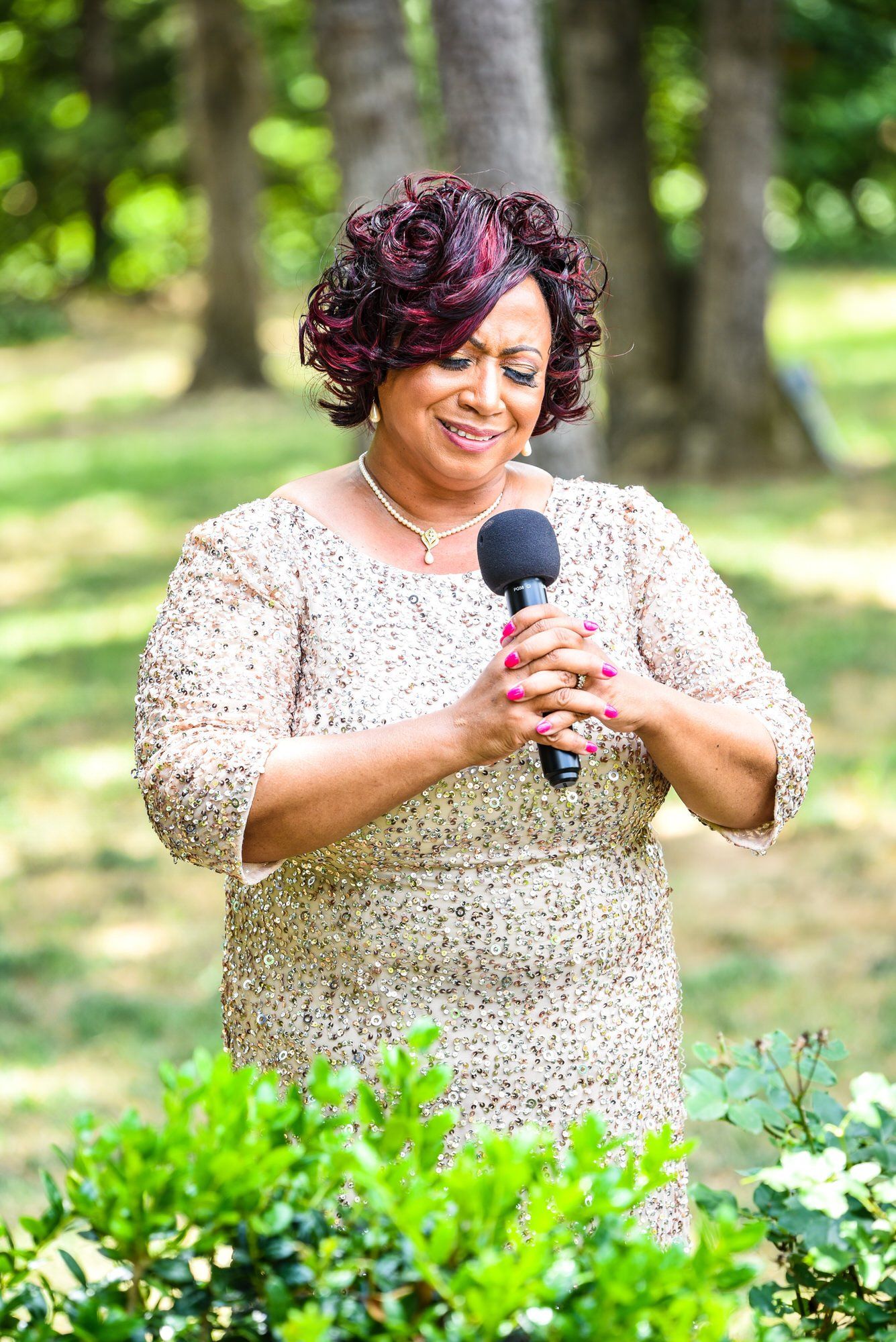 a woman in a dress is holding a microphone in a park .