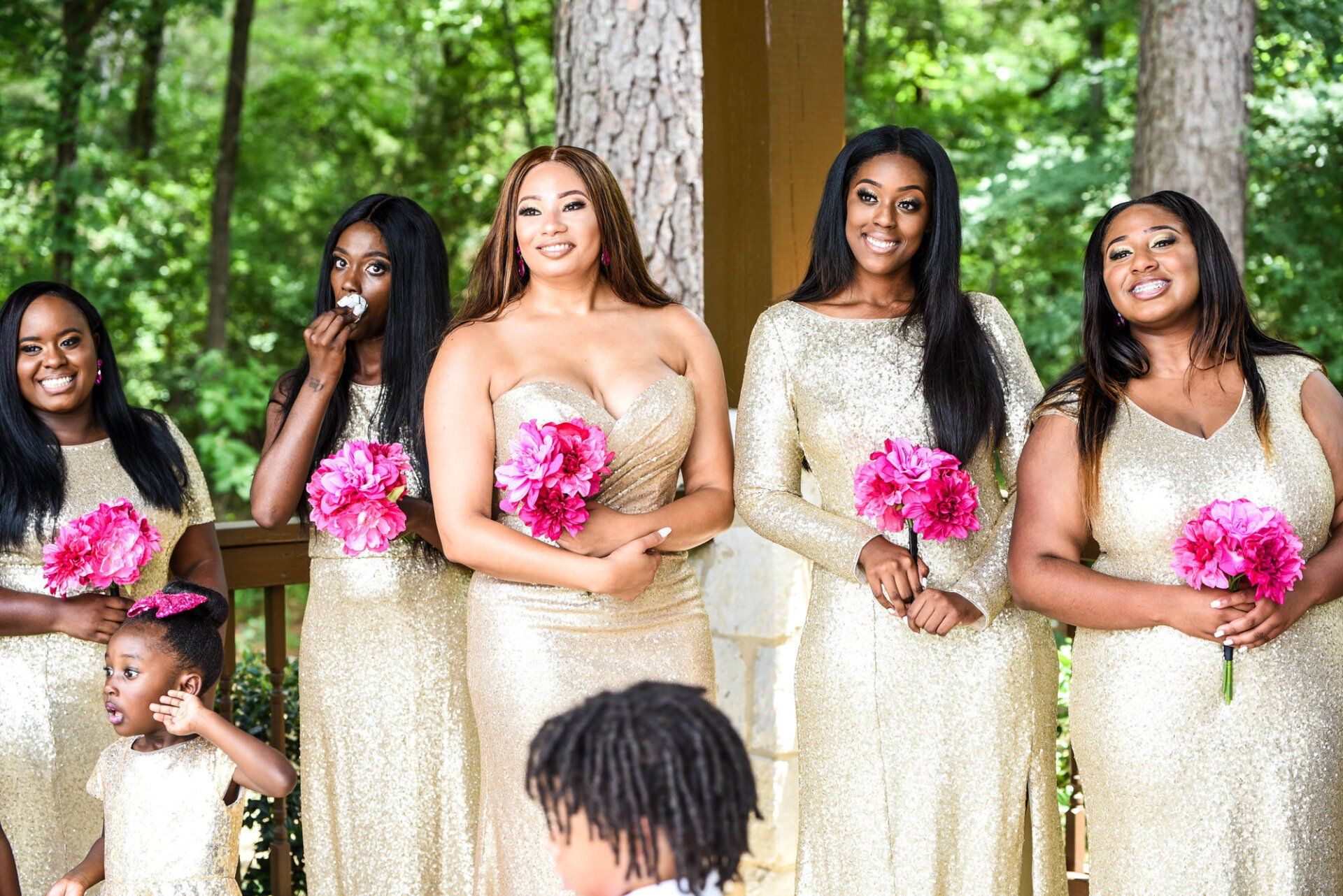 a group of women in gold dresses are standing next to each other holding pink flowers .