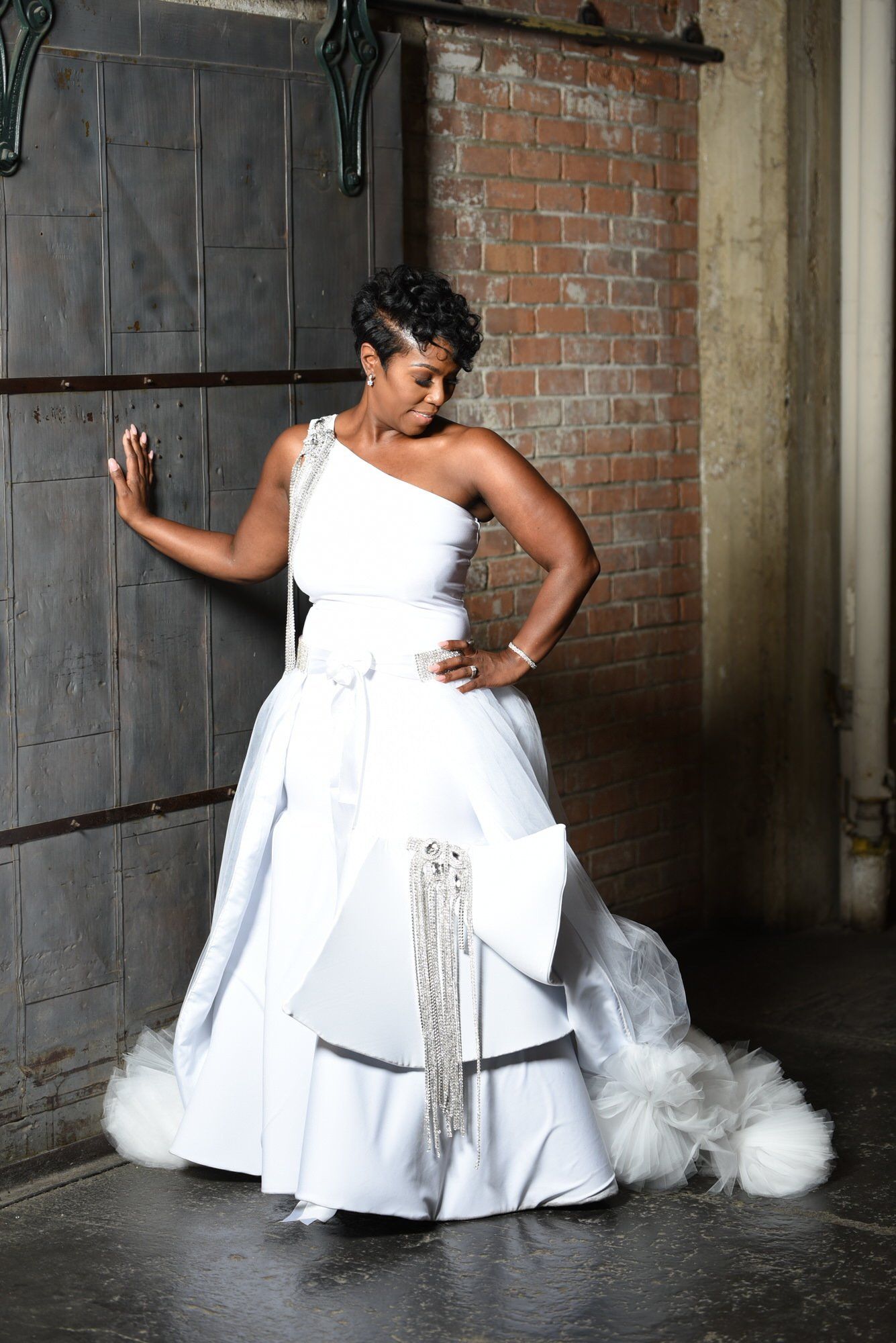 a woman in a white wedding dress is leaning against a brick wall .