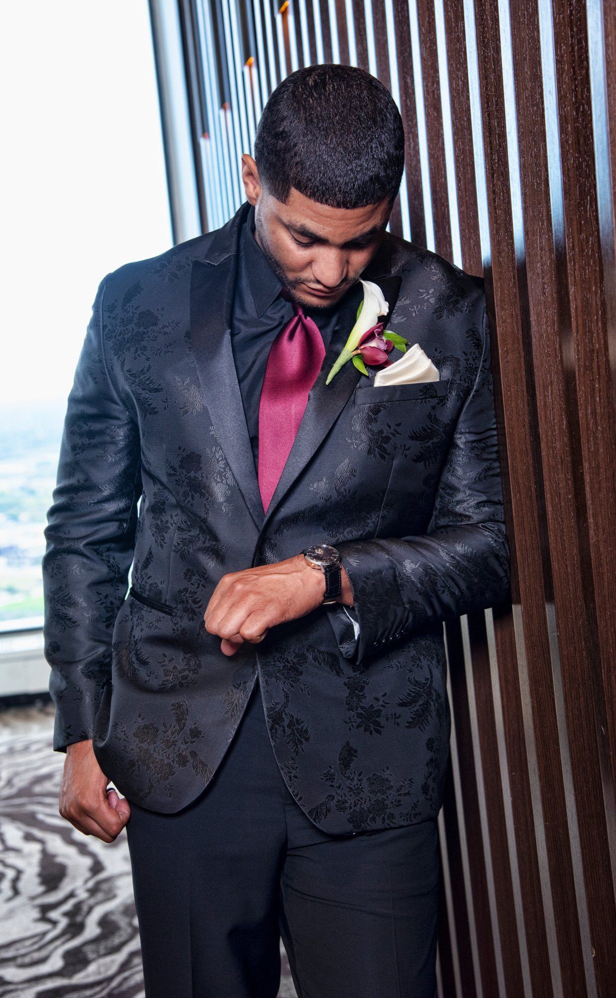 a man in a black suit and red tie is leaning against a wall .