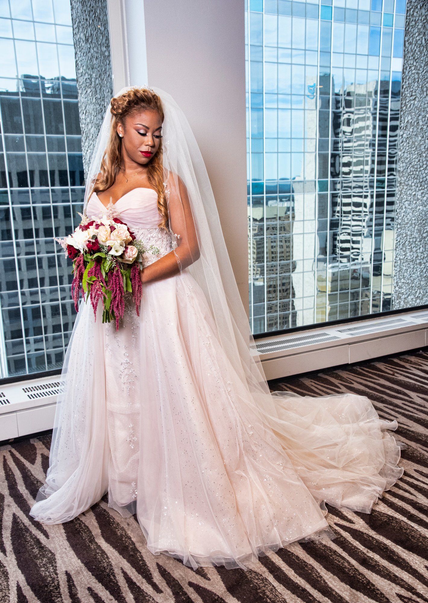 a bride in a wedding dress is standing in front of a window holding a bouquet of flowers .