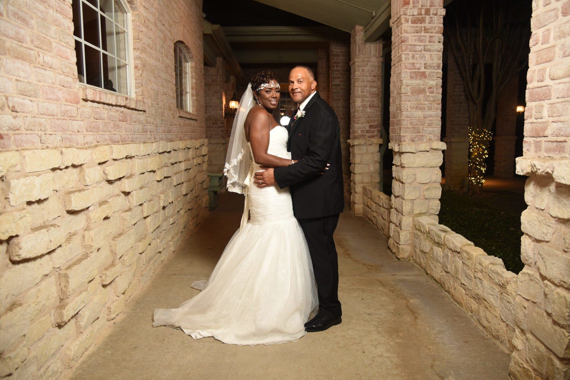 a bride and groom are posing for a picture in front of a brick wall .