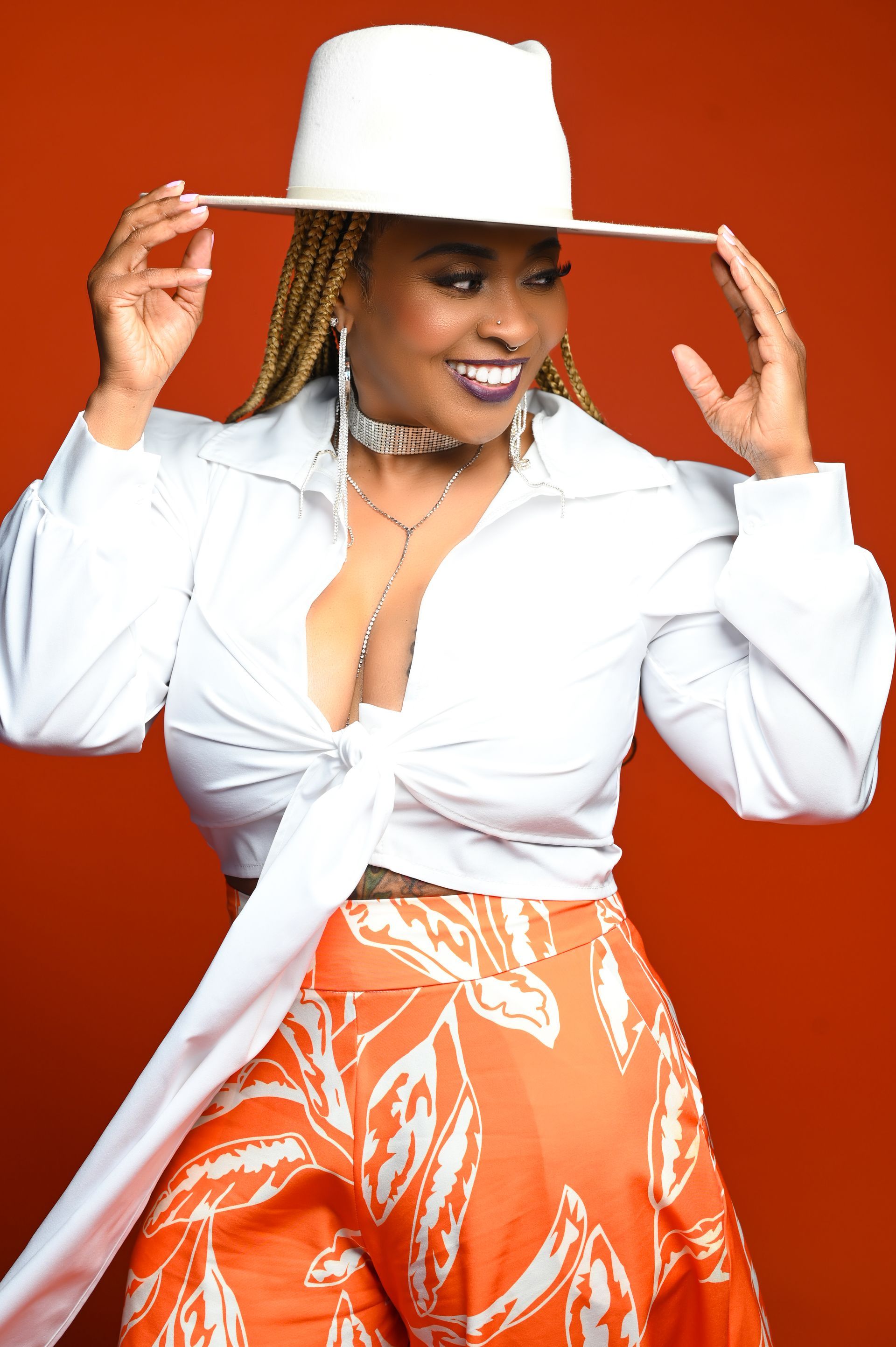 a woman wearing a white hat and orange pants is standing in front of an orange background .
