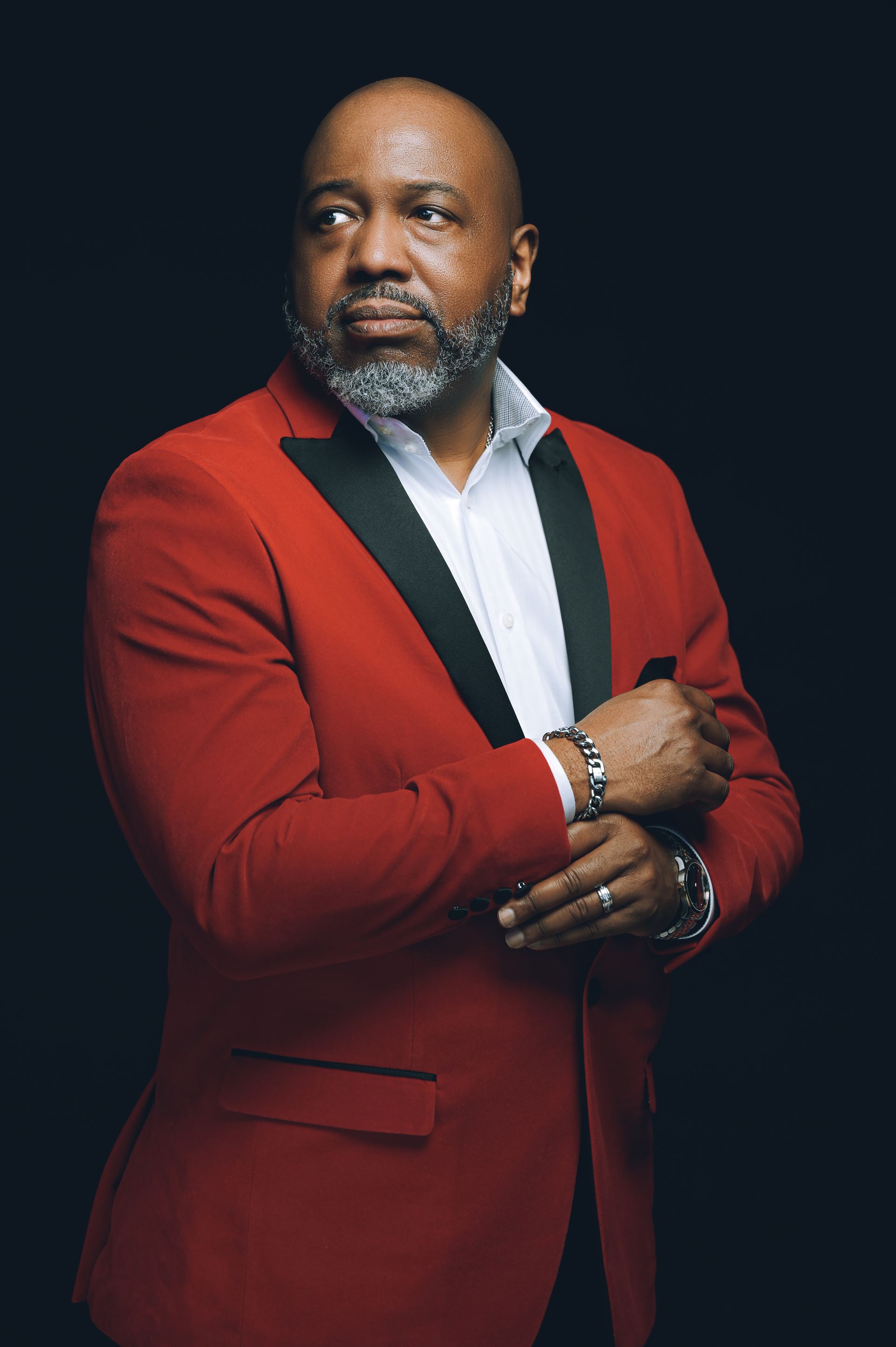 a man in a red tuxedo and white shirt is standing with his arms crossed .