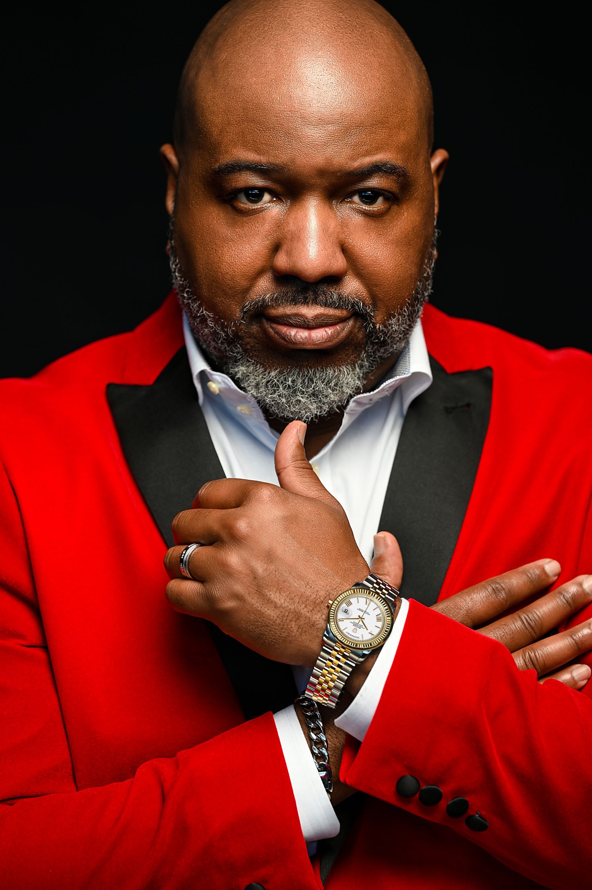 the man is wearing a red jacket and a black tuxedo and has a watch on his wrist .