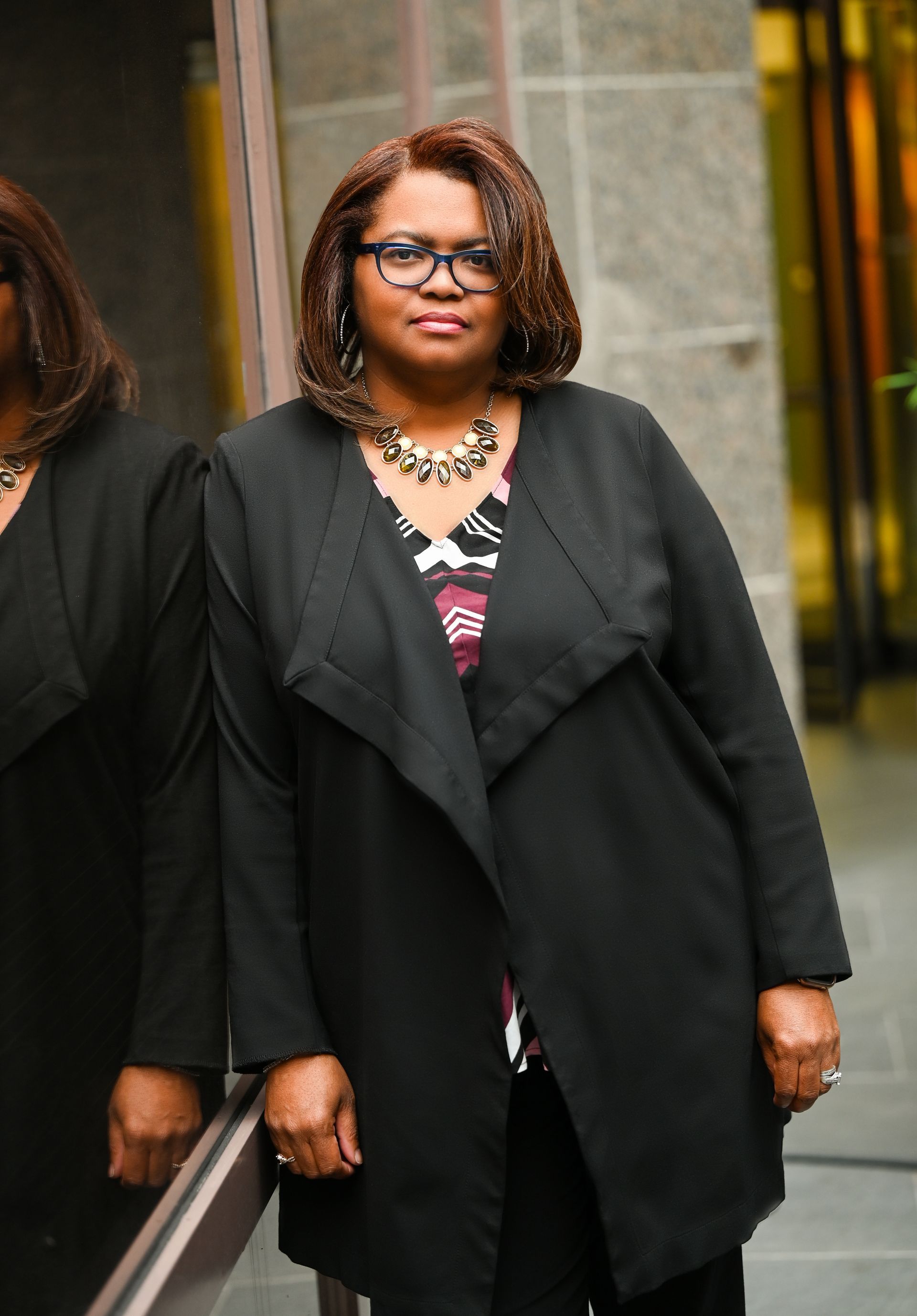 a woman in a black coat and glasses is standing in front of a mirror .