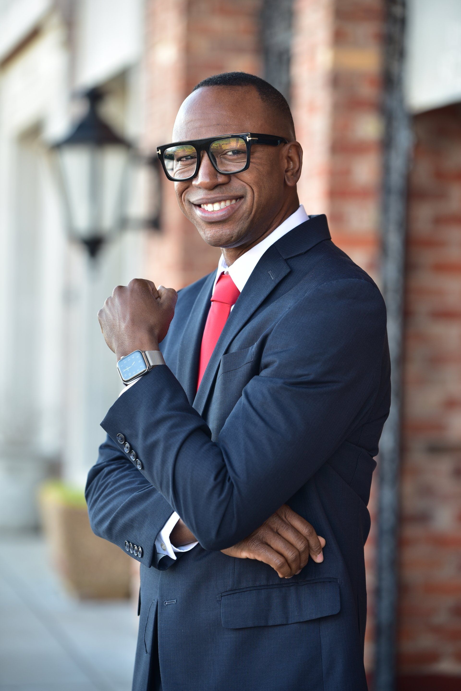 a man in a suit and tie is standing with his arms crossed and smiling .