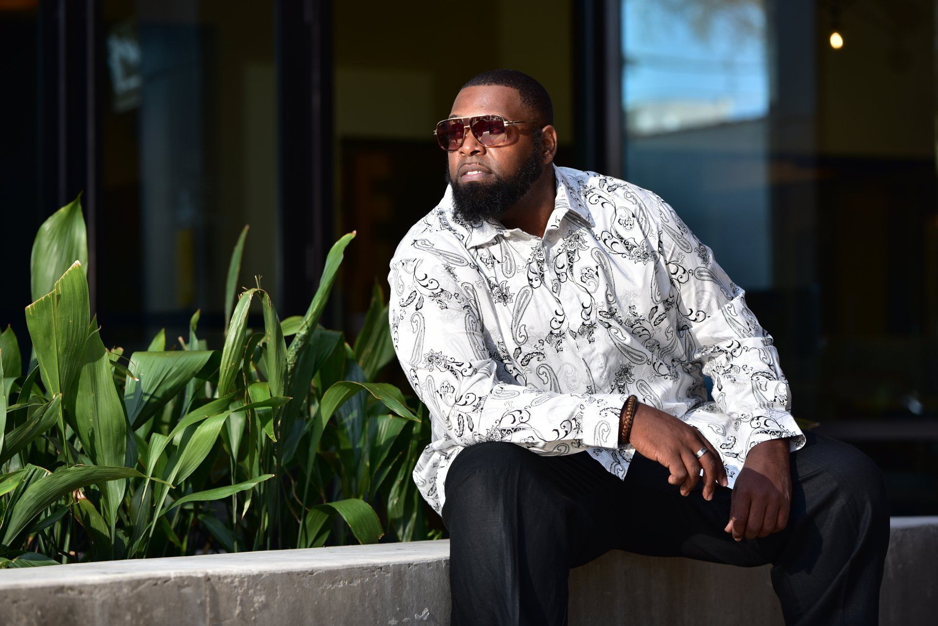 a man wearing sunglasses and a white shirt is sitting on a wall .