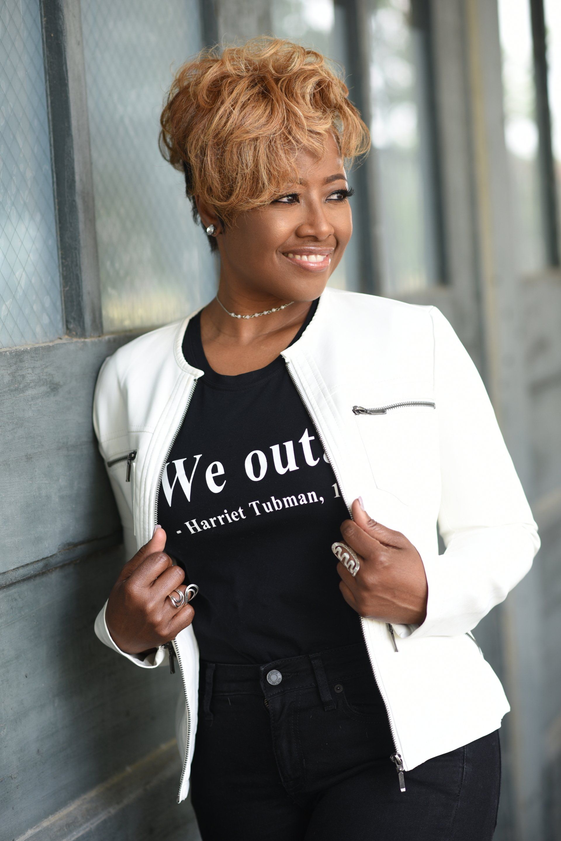 a woman wearing a black t-shirt that says `` we out '' is leaning against a wall .