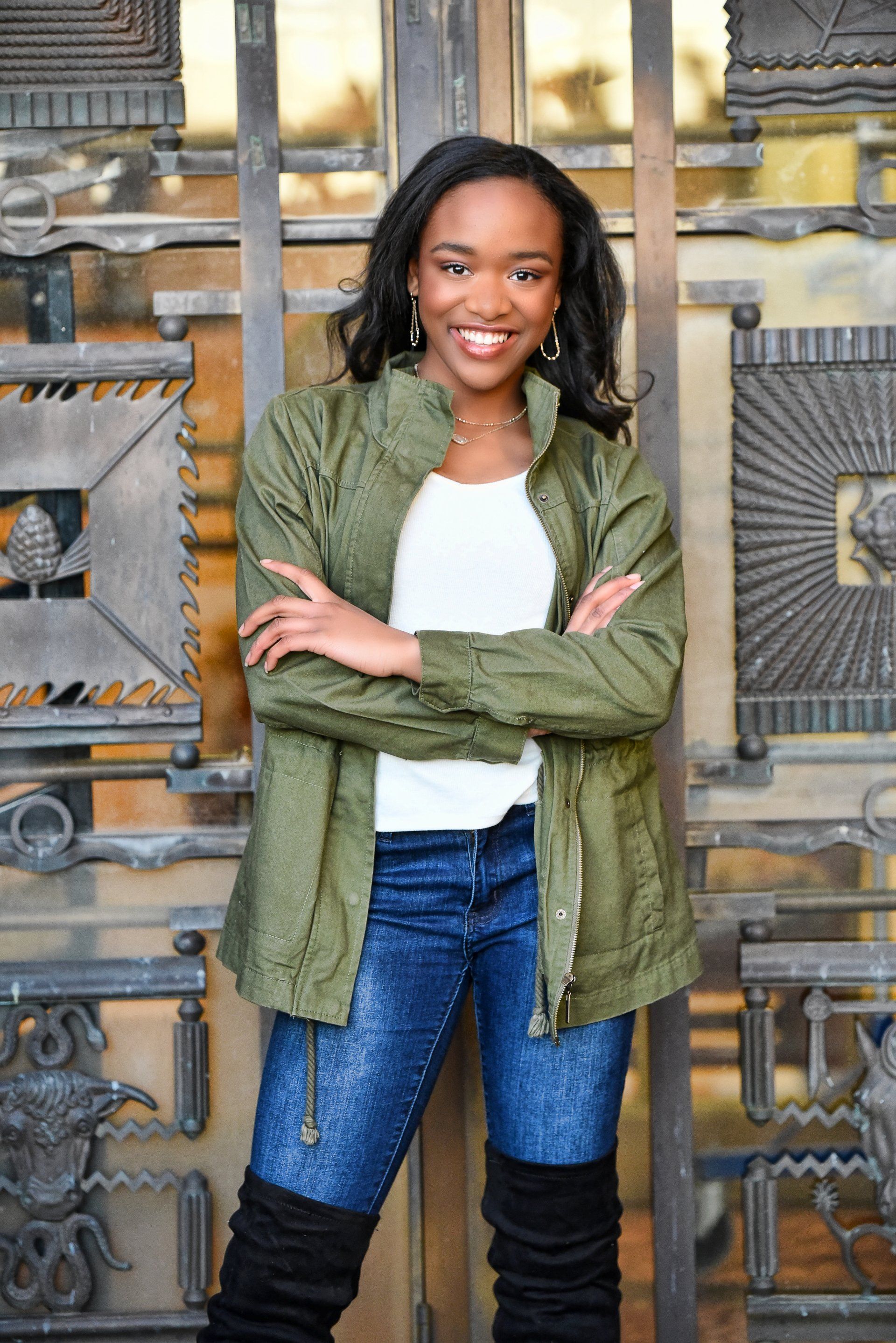 a woman in a green jacket and over the knee boots is standing in front of a building .