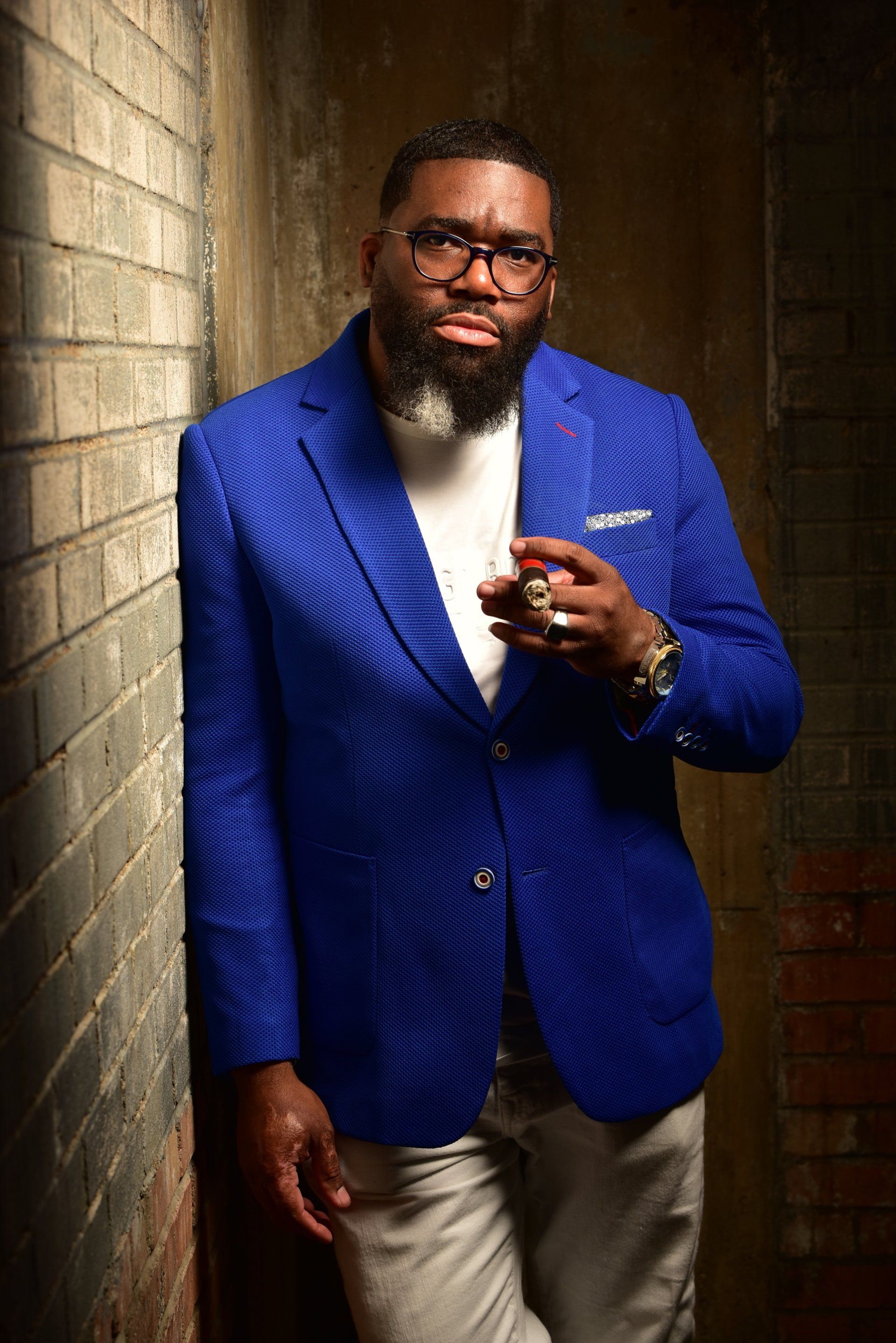 a man in a blue jacket and glasses is leaning against a brick wall .