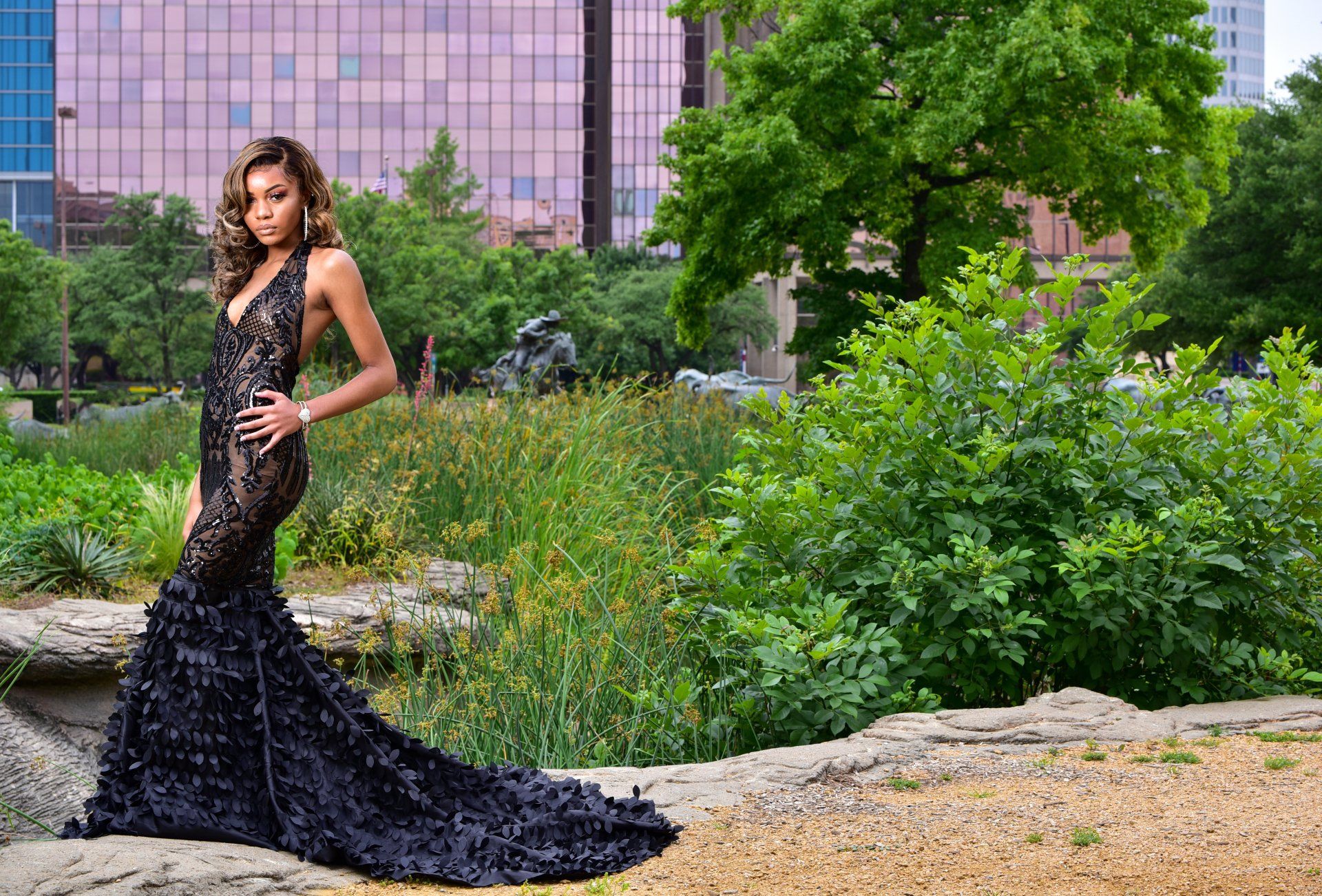 a woman in a black dress is standing on a rock in a park .