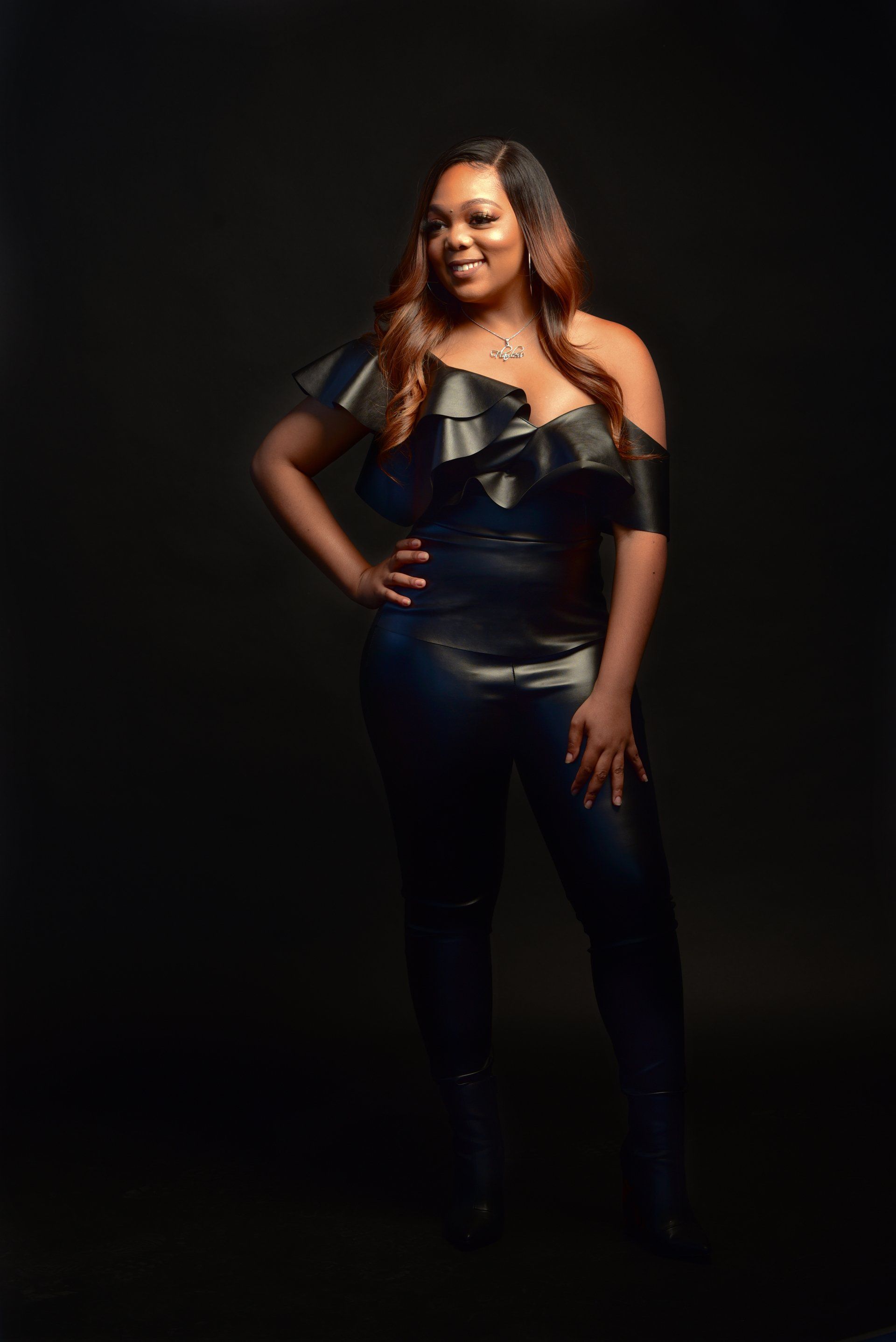 a woman in a black leather jumpsuit is standing in front of a black background .