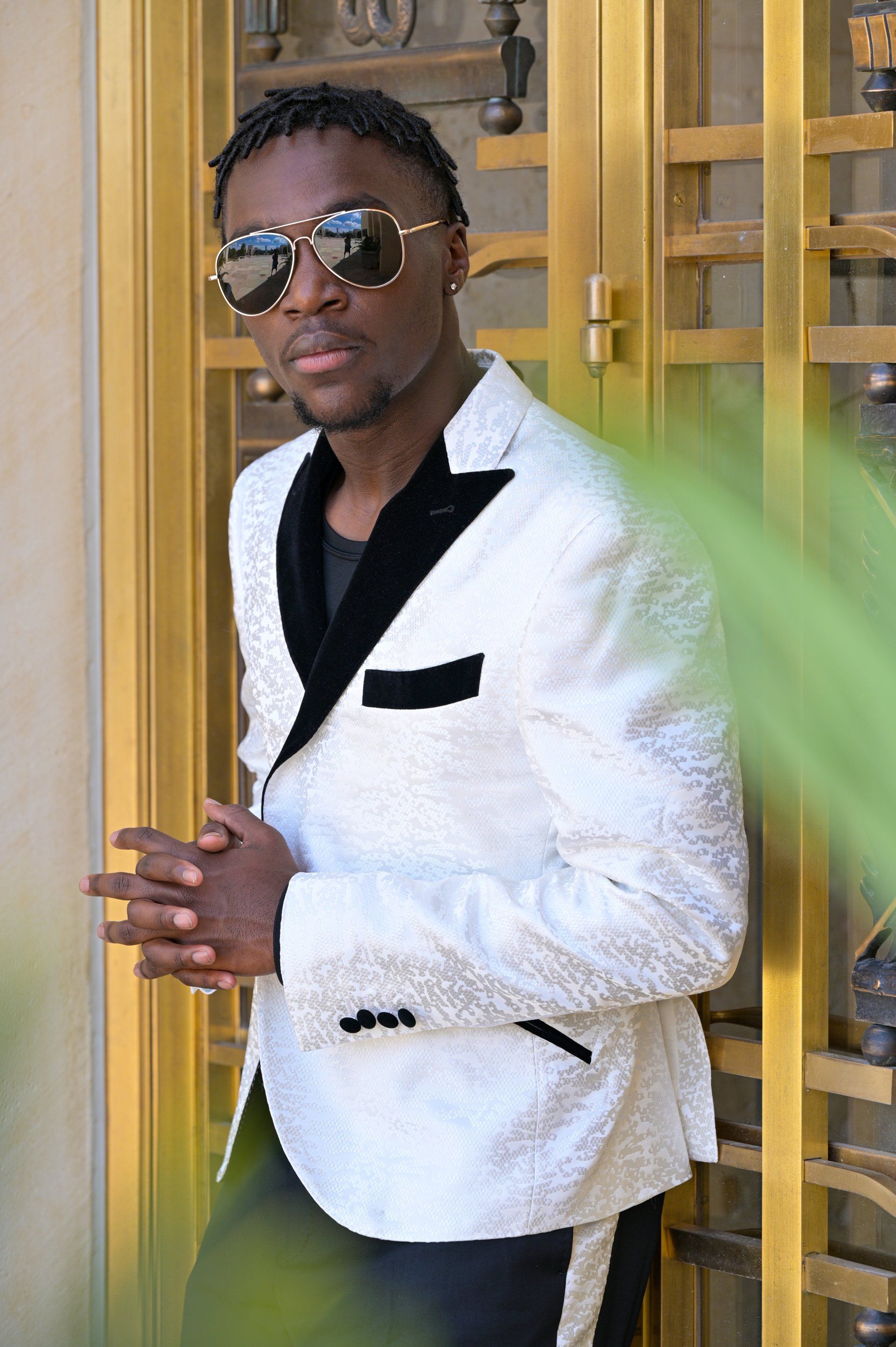 a man in a white suit and sunglasses is leaning against a door .