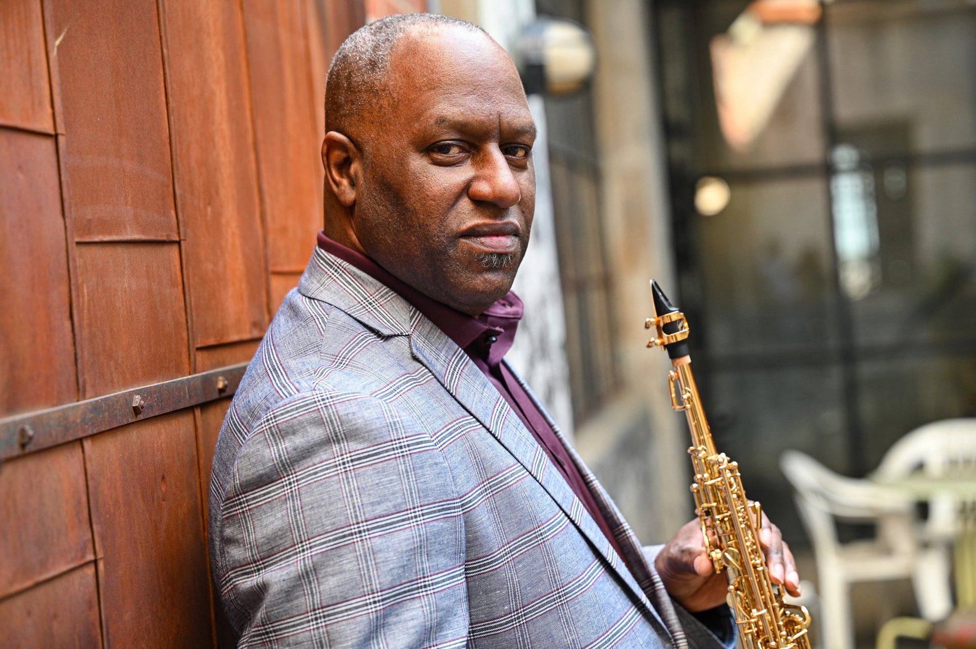 a man in a suit is holding a saxophone and leaning against a wall .