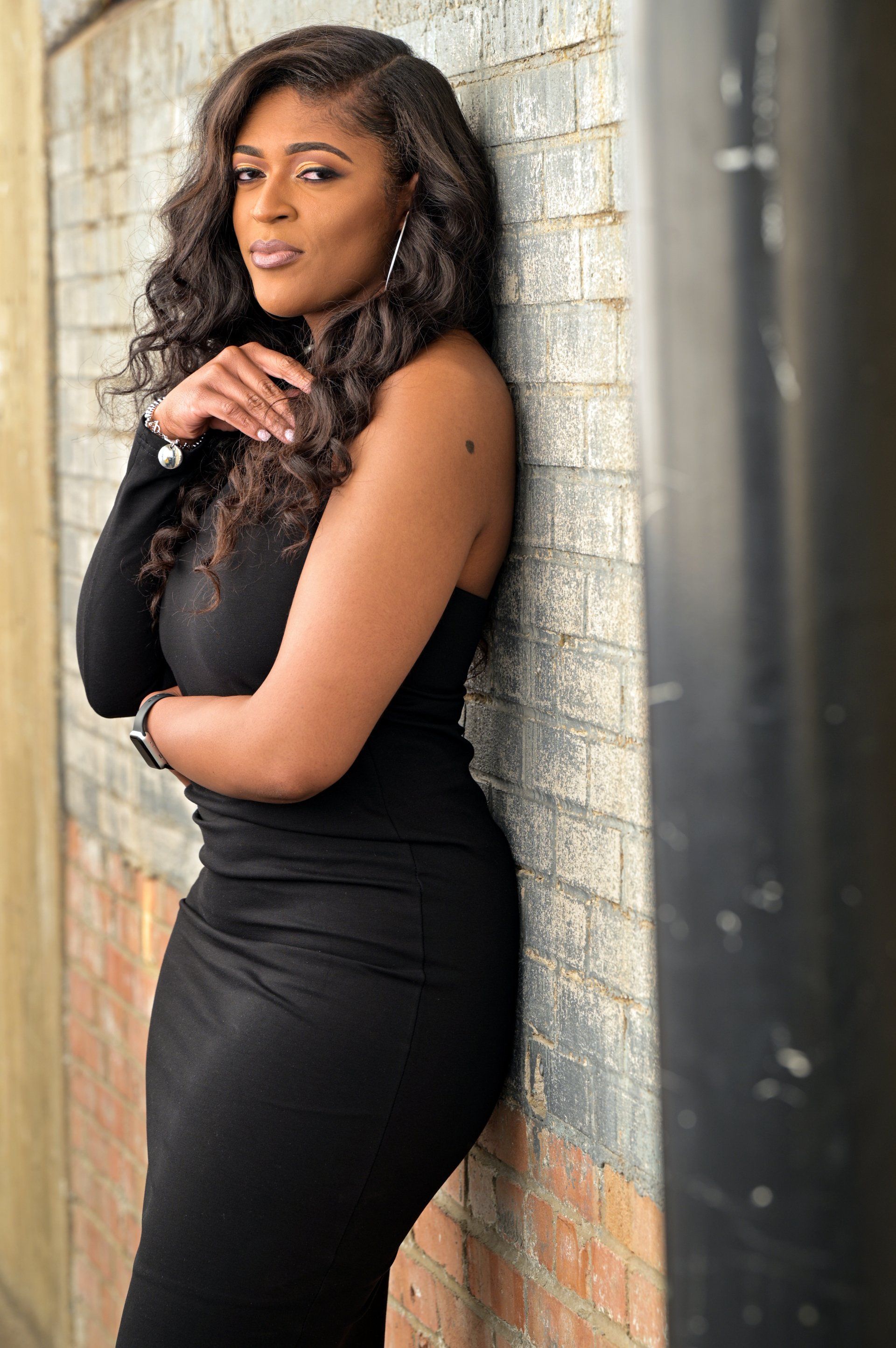 a woman in a black dress is leaning against a brick wall .