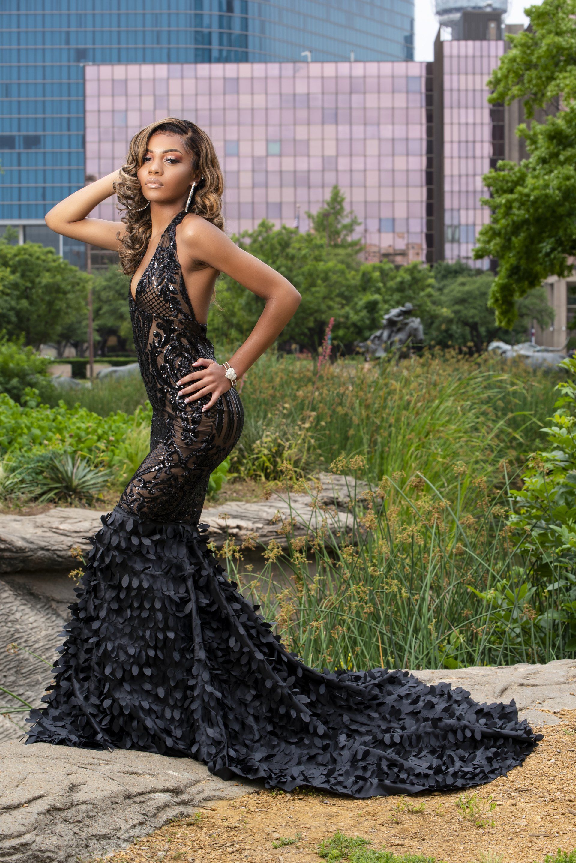 a woman in a black dress is standing on a rock in a park .