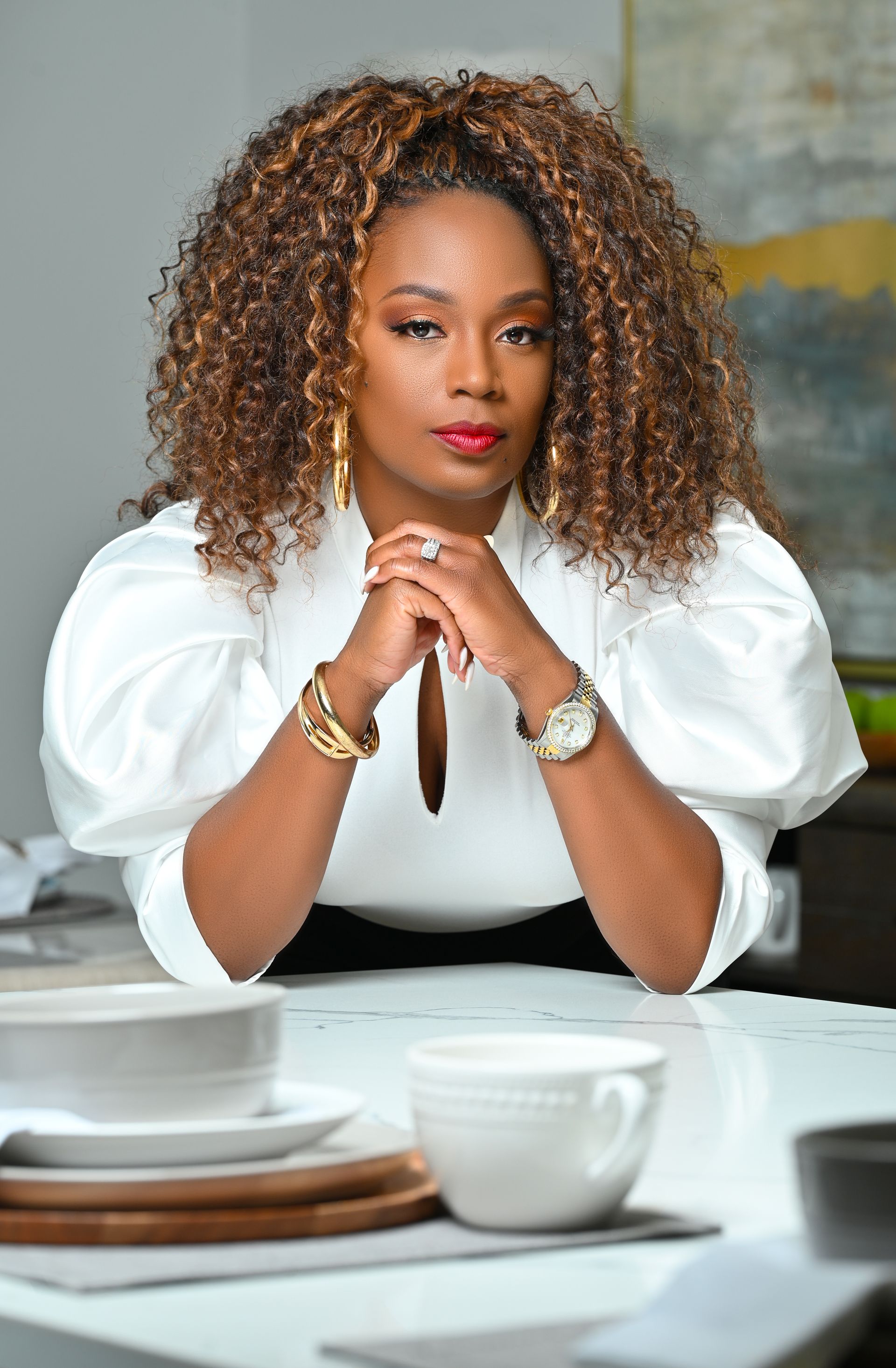 a woman with curly hair is sitting at a table with her hands folded .