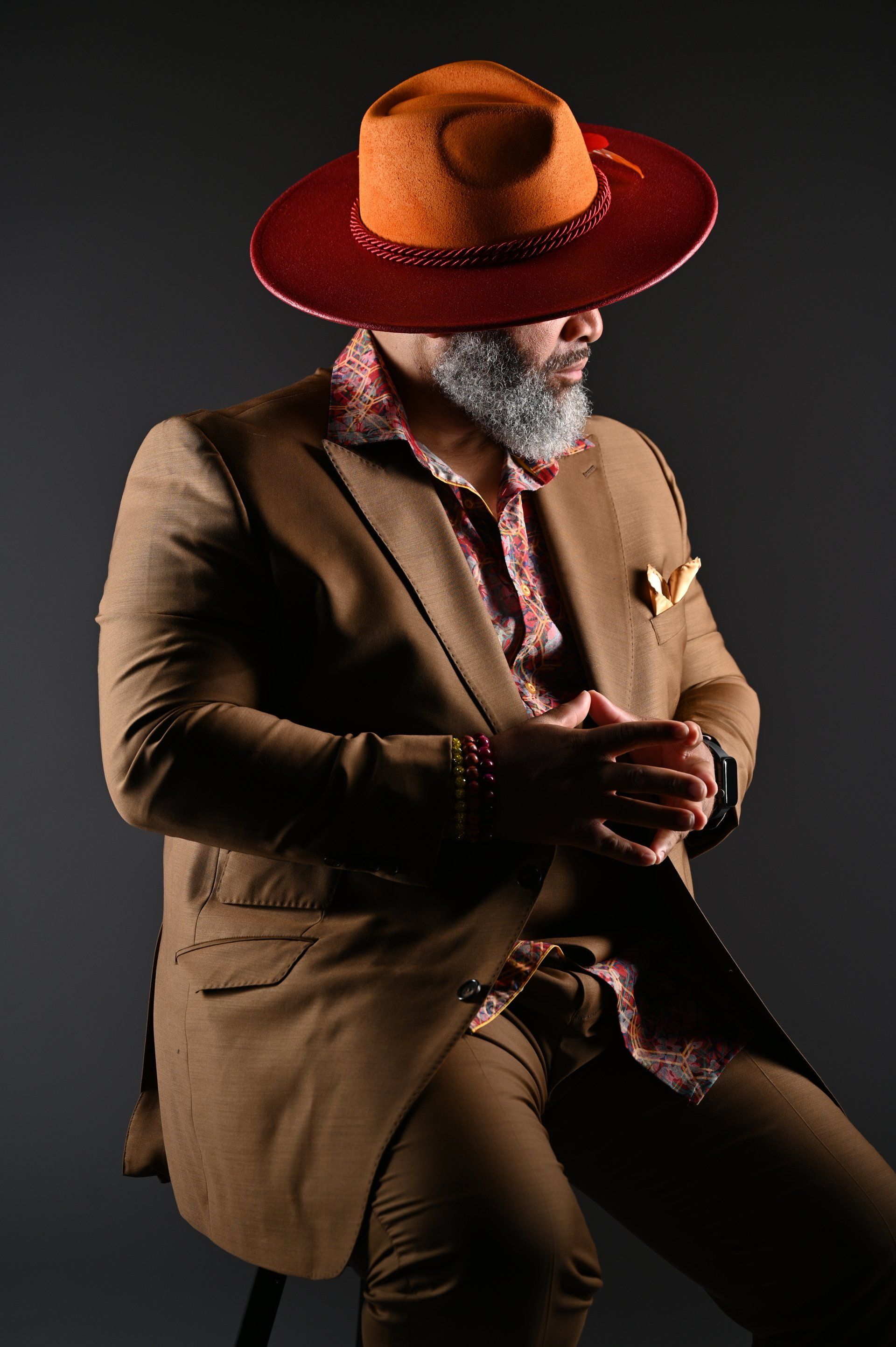 a man in a suit and hat is sitting on a stool .