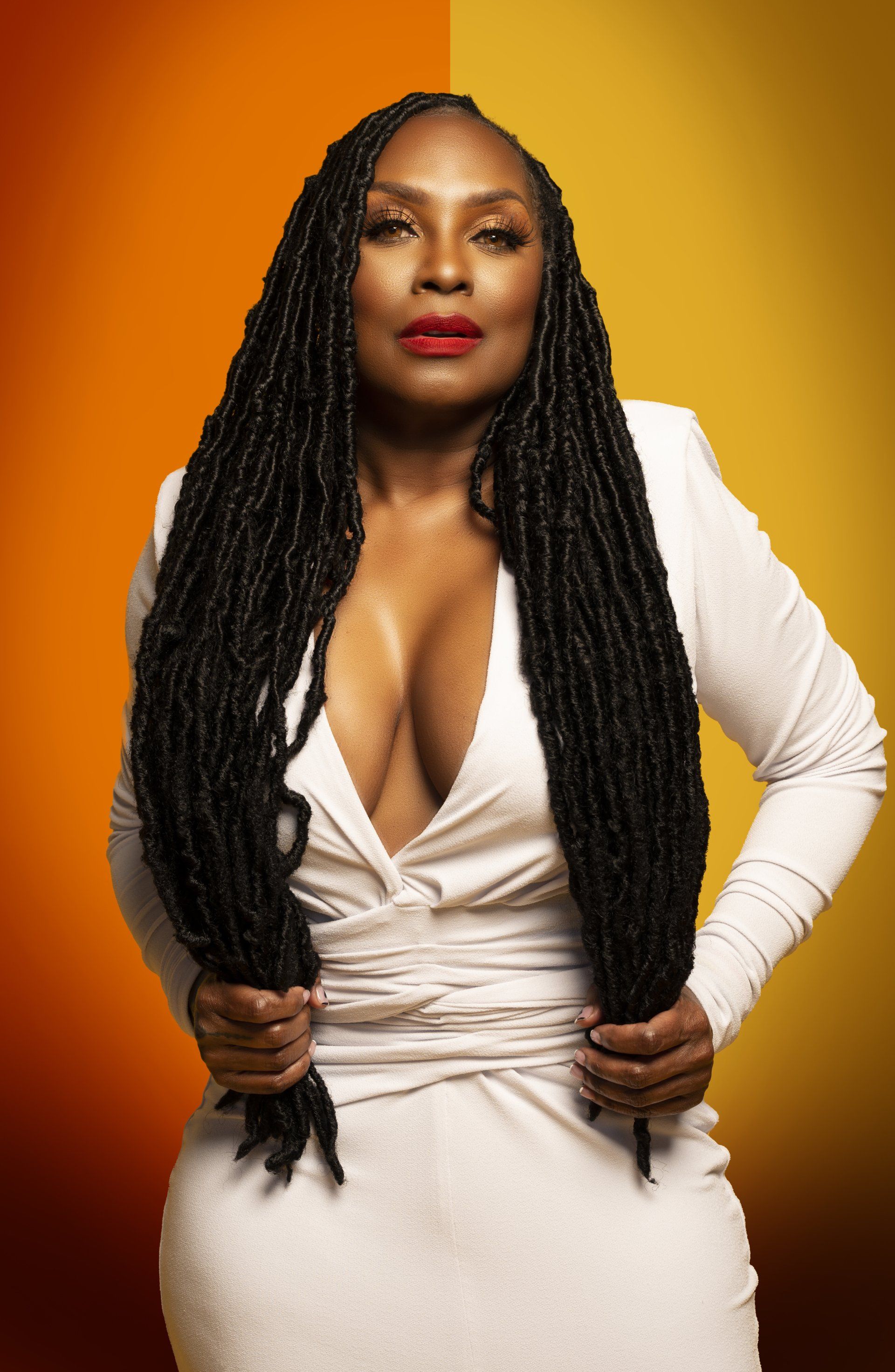 a woman with dreadlocks is wearing a white dress with a plunging neckline .