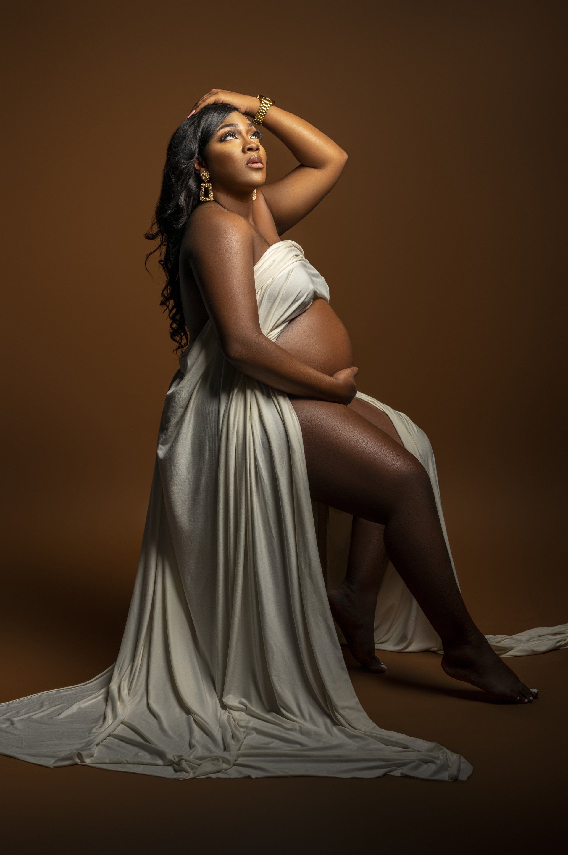 a pregnant woman in a white dress is sitting on the floor holding her belly .