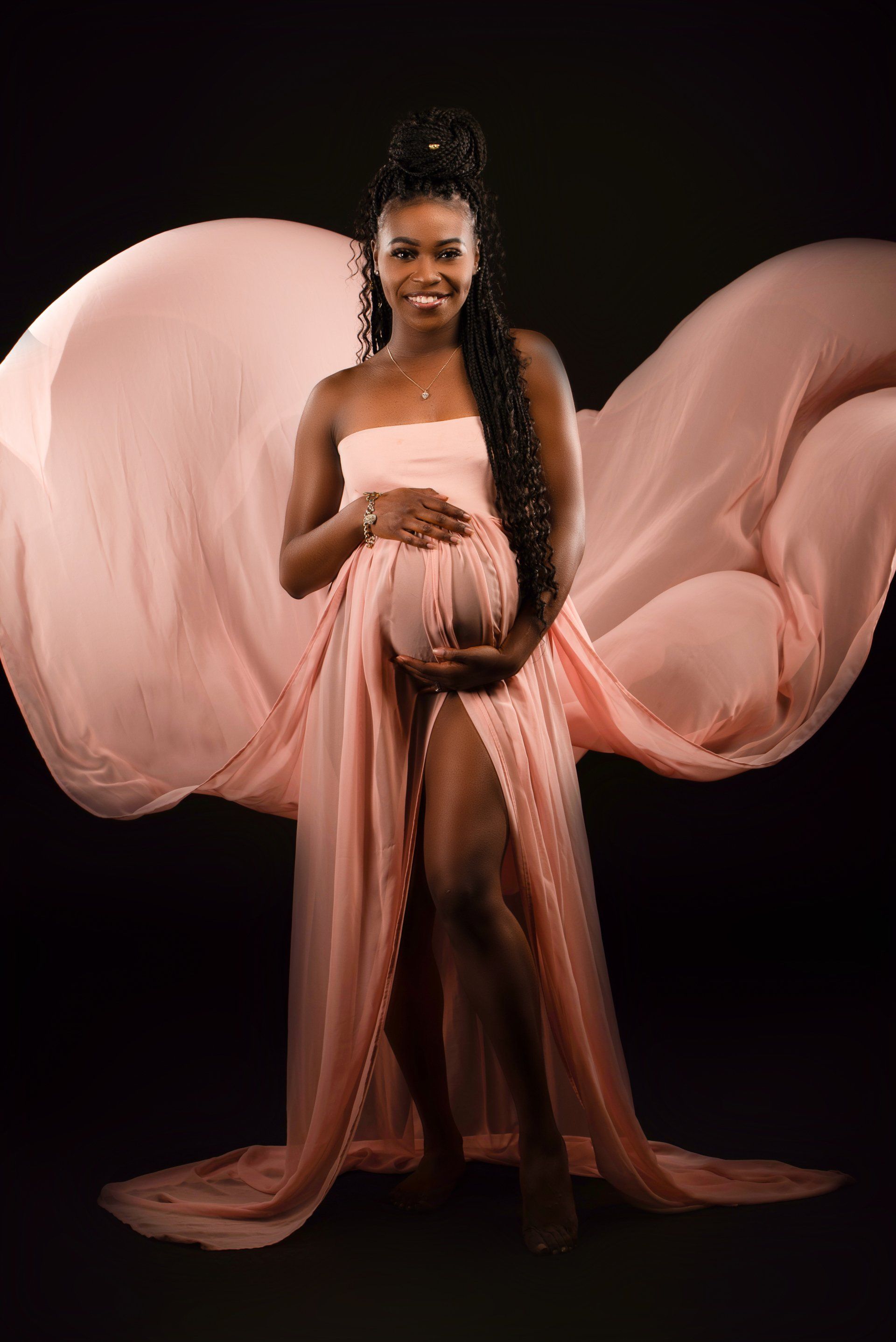 a pregnant woman in a pink dress is standing in front of a black background .