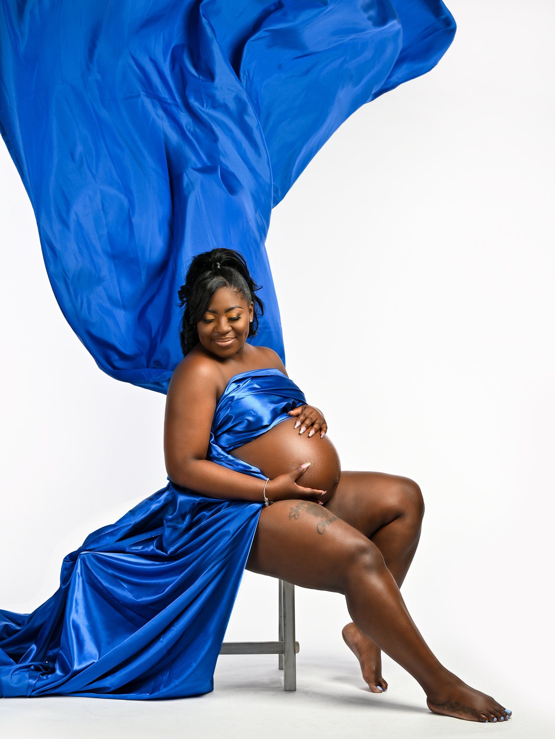 a pregnant woman in a blue dress is sitting on a stool .