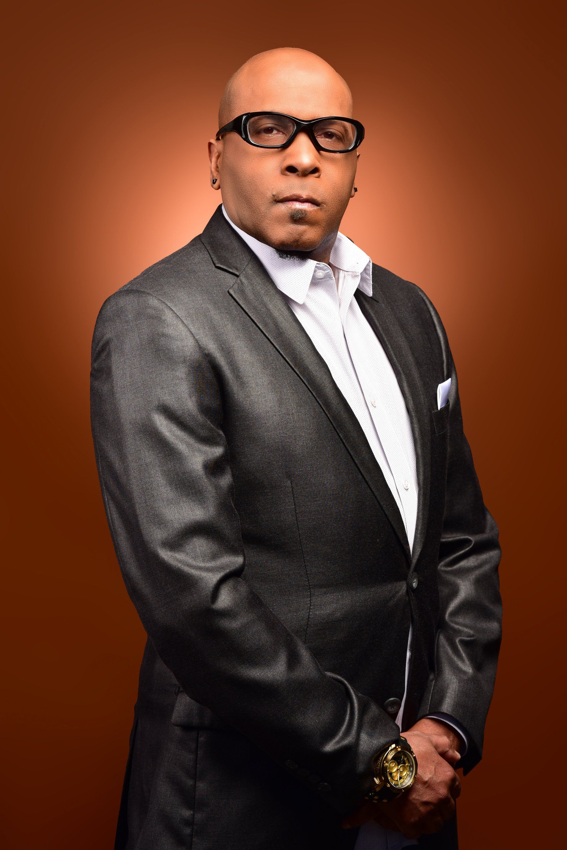a man in a suit and glasses is standing in front of a brown background .