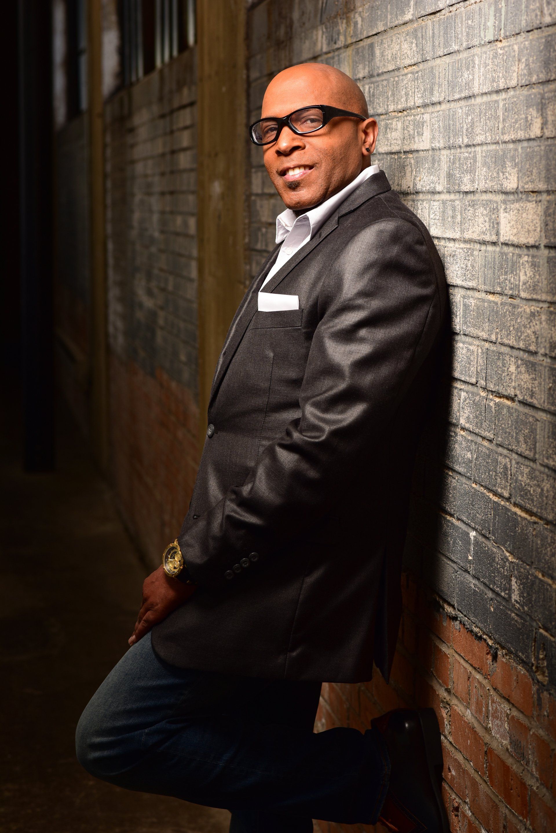 a man in a suit and glasses is leaning against a brick wall .