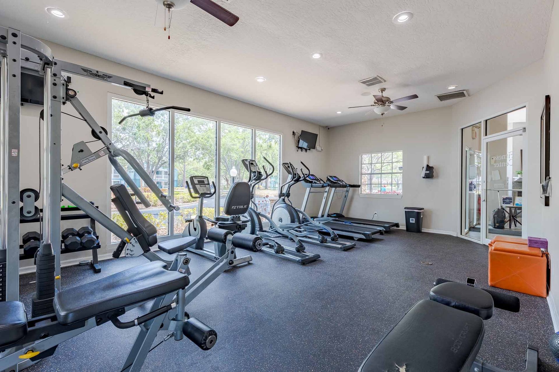 Gym with exercise machines, windows, and black rubber flooring.