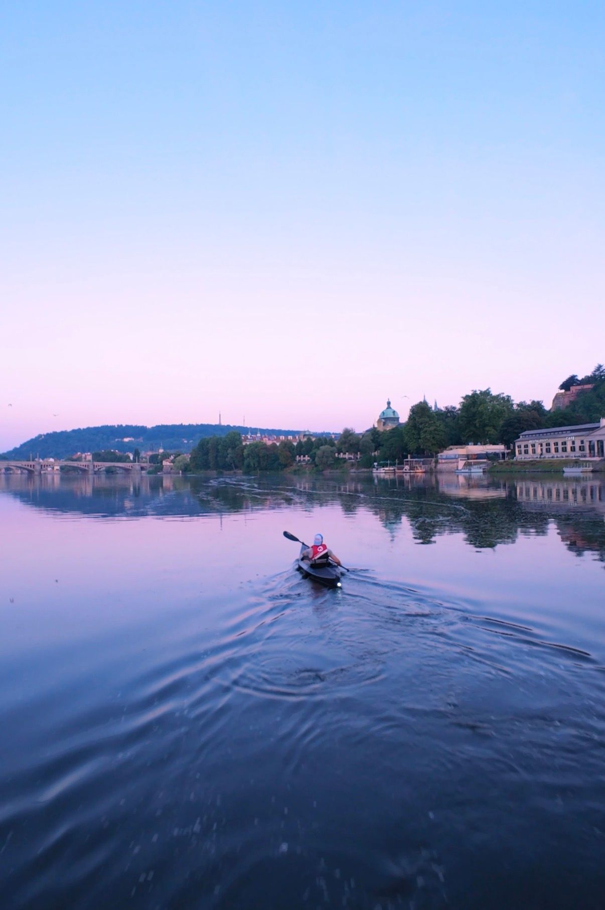 Kayaker paddling on the Vltava River at sunrise with Prague Castle views
