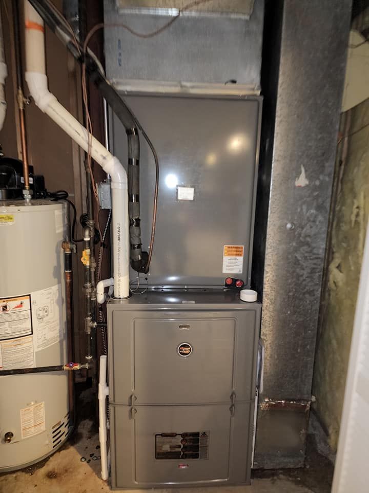 A furnace is sitting in a basement next to a water heater.