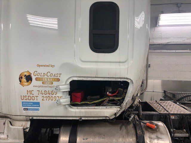 A white semi truck with the hood open is sitting in a garage.