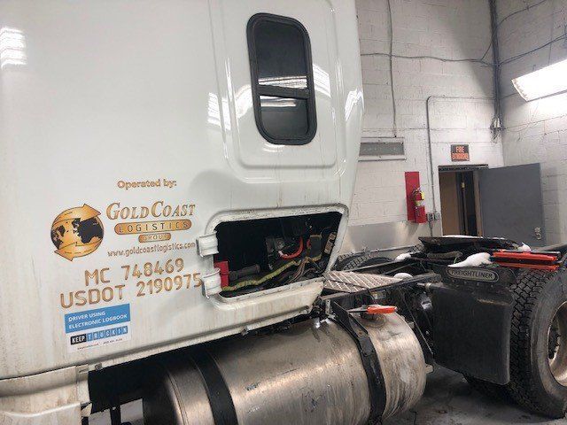 A white semi truck with the back door open is parked in a garage.