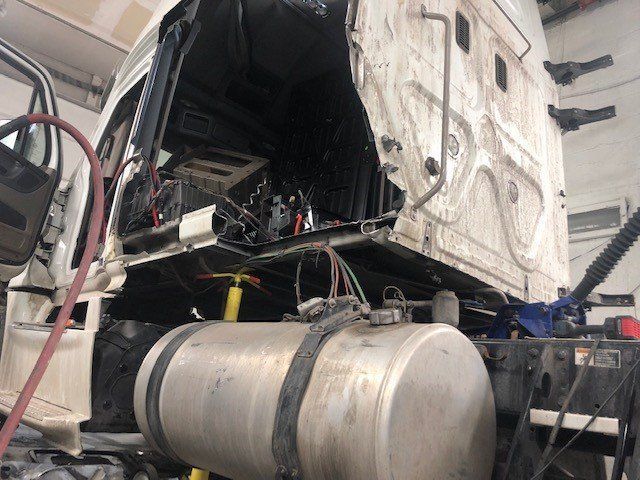 A truck is being repaired in a garage with the fuel tank removed.