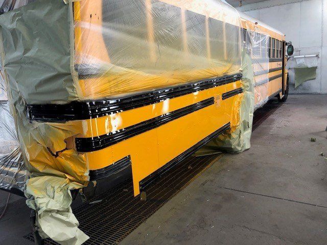 A yellow school bus is being painted in a garage.