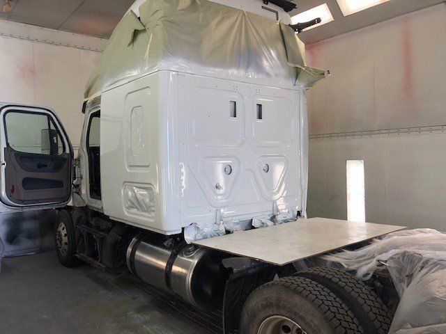 A white semi truck is being painted in a paint booth.