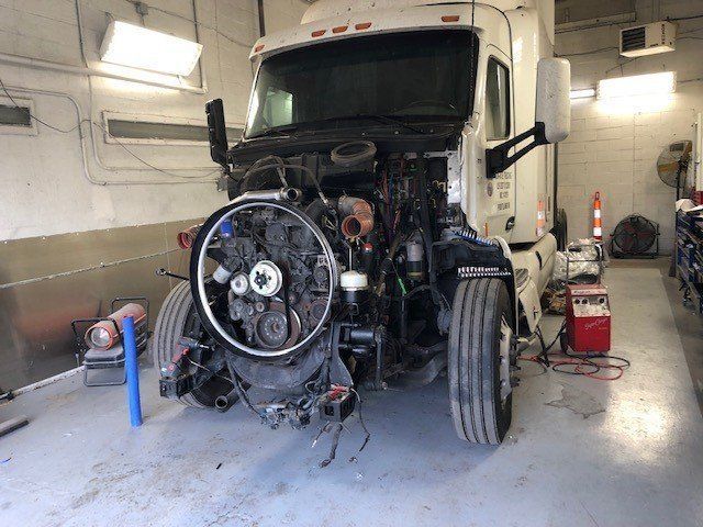 A semi truck is being repaired in a garage with its hood open.