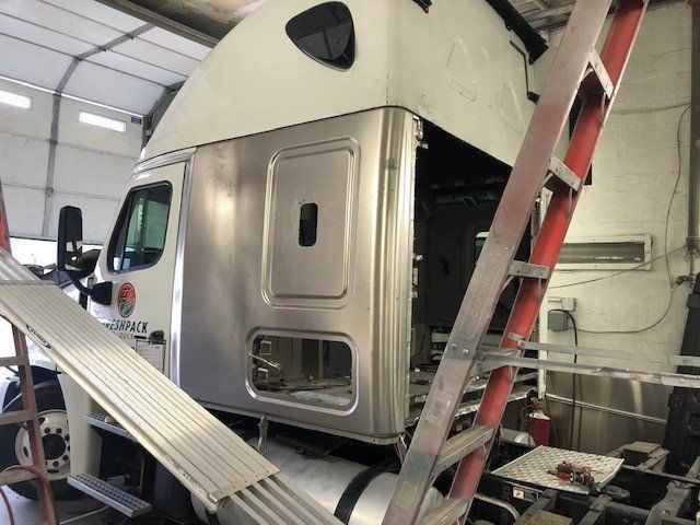 A semi truck is being repaired in a garage with a ladder.