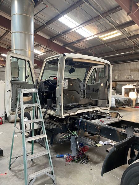 A truck is being worked on in a garage with a ladder.