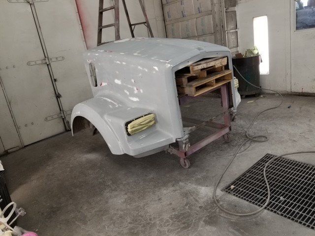 A white truck hood is sitting on a cart in a garage.