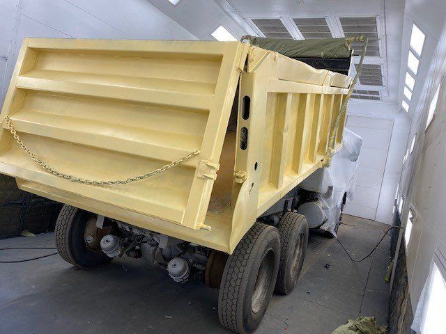 A yellow dump truck is sitting in a paint booth.