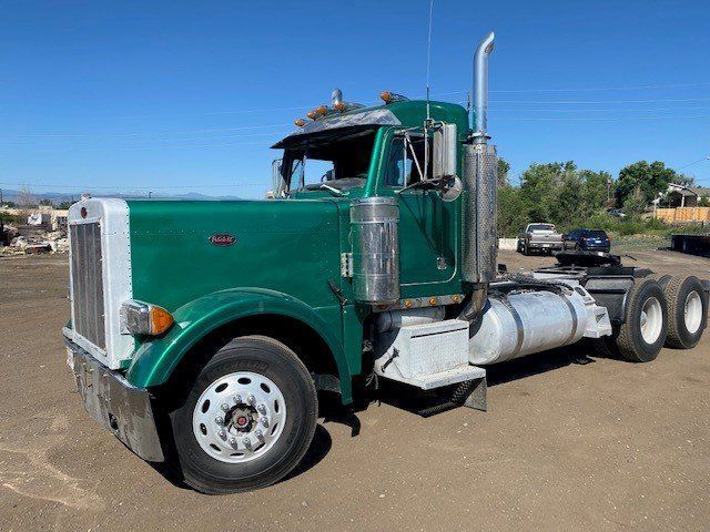 A green semi truck is parked in a dirt lot.