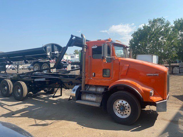 An orange dump truck is parked in a dirt lot.