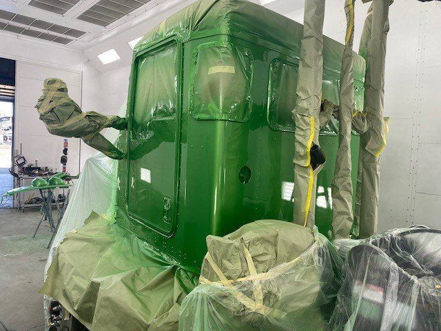 A green truck is being painted in a garage.