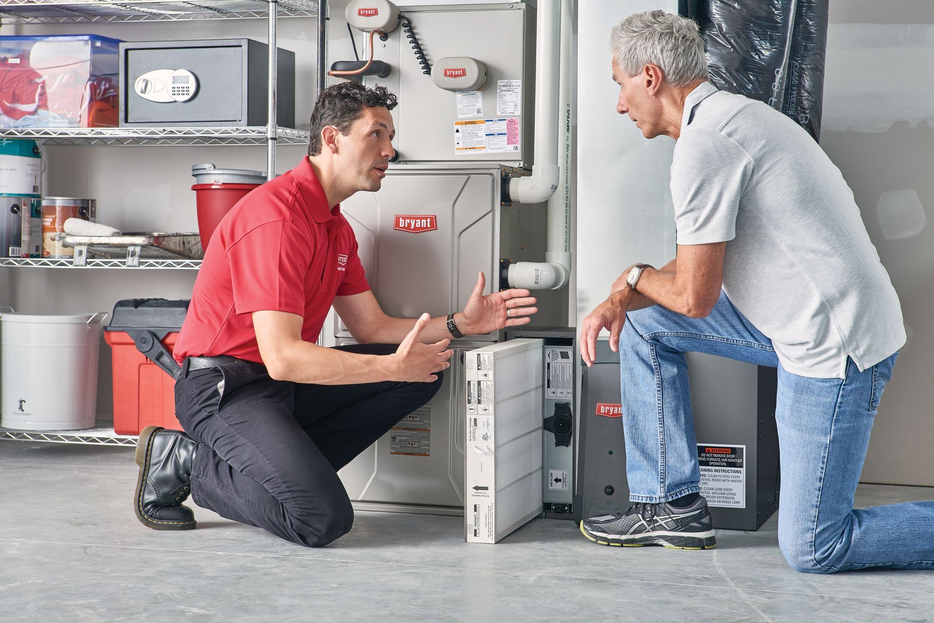 HVAC technician in red shirt and customer inspecting a furnace in a basement.